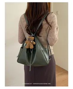 Green convertible bucket backpack with drawstring closure and a teddy bear charm, worn from behind