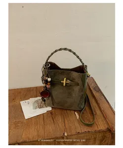 Olive green suede and leather bag with braided handle, gold clasp and wooden charm on a table