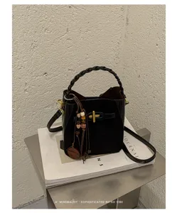 Black bucket bag displayed with a braided handle, gold T-shaped clasp, wooden bead charms and strap