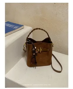 Brown suede bucket bag with braided handle, leather strap, metal clasp and hanging tassel