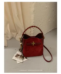 Red suede-texture bag with braided handle, gold T clasp and long shoulder strap displayed on a neutral set