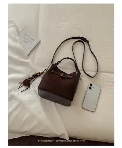 Flat lay showing a brown suede bucket bag with braided handle, leather trim and shoulder strap