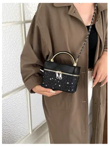 Una persona tiene una piccola borsa nera con stelle bianche, manico dorato e tracolla a catena.