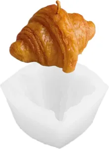Golden croissant-shaped candle with a visible wick displayed above its white silicone mold
