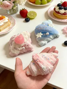 Pastel whipped-cream pieces with glitter, pearls and snowflake accents, one displayed in hand.