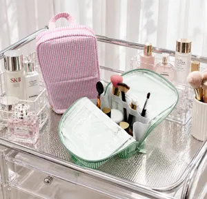 Open pink and green striped bags show clear lining and divided compartments beside cosmetics.