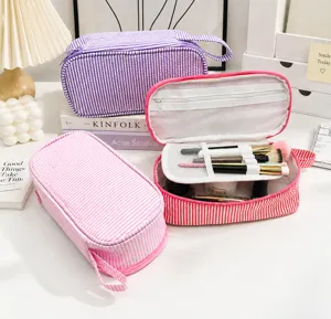 Offene gestreifte Kosmetiktasche mit Netzfächern für Pinsel, neben lila und rosa Etuis