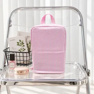 Pink-and-white seersucker stripes and top handle on a zippered pouch, displayed on a clear chair