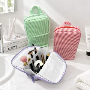 Open striped cosmetic bag showing brush holders and clear mesh compartments beside colorful cases