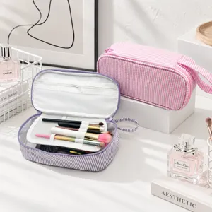 Offene gestreifte Tasche mit Netzfach und Pinselschlaufen neben einer geschlossenen rosa Tasche