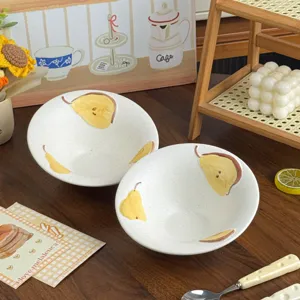 Twee witte, matte kommen met spikkels en gele perenmotieven, op een donkere houten tafel