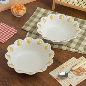 Twee matwitte kommen met geschulpte randen en handgeschilderde gele peren, op een houten tafel