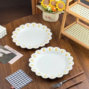 Twee matte witte borden met golvende bloemblaadjesrand en gele reliëfaccenten op een houten tafel
