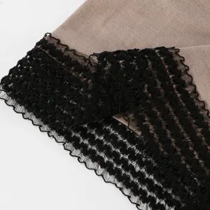 Primo piano del bordo in pizzo nero ondulato su maglia beige, con trama traforata ben visibile