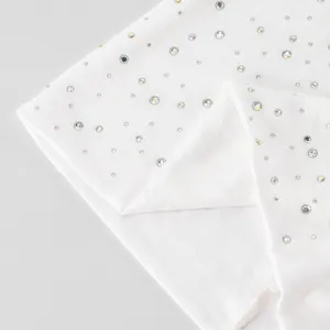 Close-up van heldere, iriserende strasssteentjes op gevouwen witte elastische breistof