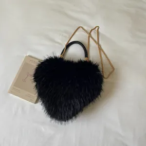 Black fluffy heart-shaped bag laid flat on white bedding, with a woven handle and gold chain strap