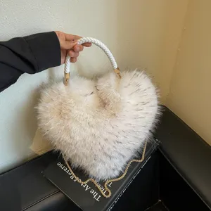 Close-up of a cream faux-fur heart bag with a braided handle and gold chain on a black book