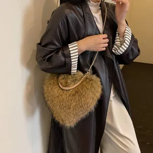 A model wears a brown furry heart-shaped bag with a braided handle and a gold-tone chain strap