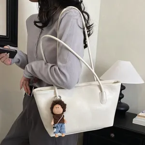 Λευκή τσάντα tote με κρεμαστό κουκλάκι με σγουρά μαλλιά, φορεμένη στον ώμο σε εσωτερικό χώρο