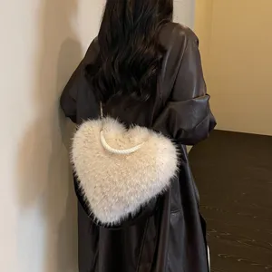 Rear view of a model carrying a fluffy ivory heart bag with a braided handle and chain strap