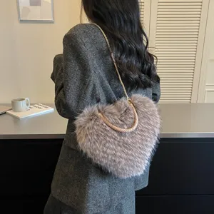 A woman wears a heart-shaped, fluffy taupe bag with a gold chain strap and braided handle