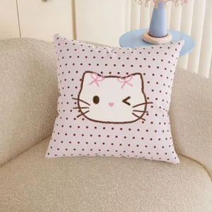 Close-up of a pink square cushion with brown polka dots and a bow-wearing cartoon cat on a sofa