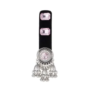 Close-up of an ornate silver-tone medallion with a pink stone and dangling bell charms on velvet