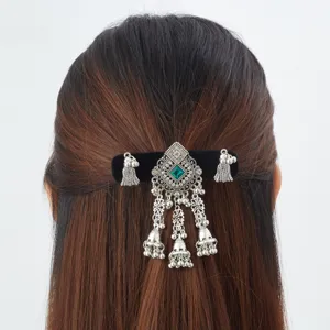 Back view of half-up hair with an ornate silver clip, green gem, and dangling bell tassels