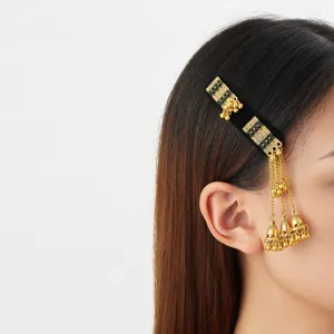 Close-up of a gold hair ornament worn beside the ear, with green accents and dangling bell tassels