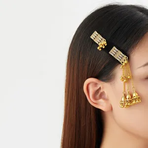 Close-up of a gold filigree hair ornament with bell charms and chain tassels worn in dark hair