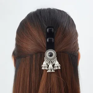 Rear view of dark hair with a black velvet clip, silver medallion and dangling bell charms