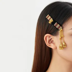 Side view of a black velvet hair clip with red accents and dangling gold bells worn in the hair