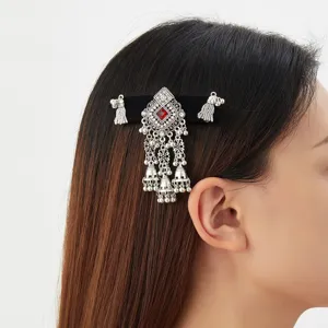 Side view of an ornate silver hair clip with a red gem, dangling bells and tassels in dark hair