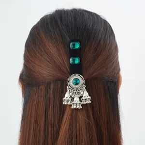 Back view of a black velvet hair clip with green stones and dangling silver bell tassels