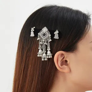 Close-up of a silver geometric hair ornament with dark stones, dangling bells and tassels worn in hair