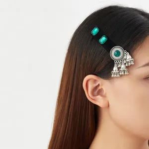 Side view of a black velvet hair clip with green gems, silver filigree and dangling bell charms