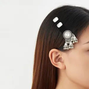 Close-up of a black velvet hair clip with clear stones and silver bell tassels worn by a model