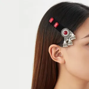 Side view of a black velvet hair clip with red stones, silver pendant and dangling bell tassels