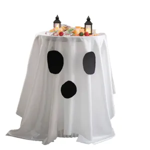 White ghost-shaped Halloween tablecloth with black face patches, draped over a table with treats