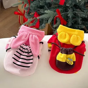 Pink bunny-ear and red bee fleece pet tops with decorative pockets, displayed by a Christmas tree