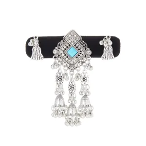 Close-up of a silver-tone ornament with a blue square stone, rhinestones, bells and tassels