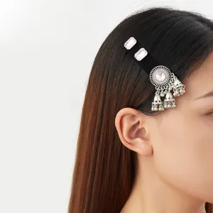 Side view of a black velvet hair clip with pink stones and dangling silver bell tassels