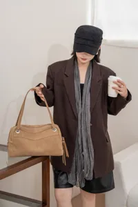 Lifestyle view of a tan suede-textured handbag with double handles and silver hardware