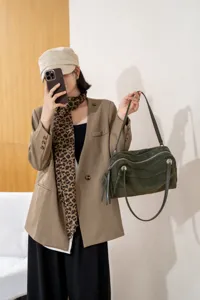 Lifestyle view of a woman holding a dark green suede bag with a shoulder strap against a bright wall