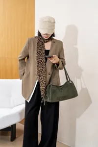 Lifestyle view of a woman carrying a green suede-textured handbag with twin handles and hardware