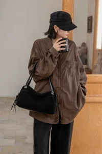 A woman carries a black suede-textured bag with leather trim and fringe in a casual outfit