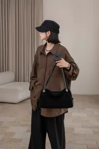 Black suede shoulder bag worn crossbody, showing its curved shape and silver-tone hardware