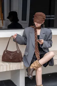 Brown suede-textured handbag with leather handles and a tassel zipper, displayed on a stone bench