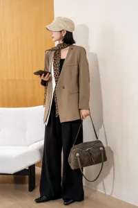 Dark brown suede handbag carried with a camel blazer and black trousers in a relaxed outfit