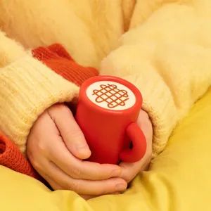 Roter Tassen-Handwärmer mit rundem Griff und weißem Muster oben, vor warmem Strickstoff gehalten